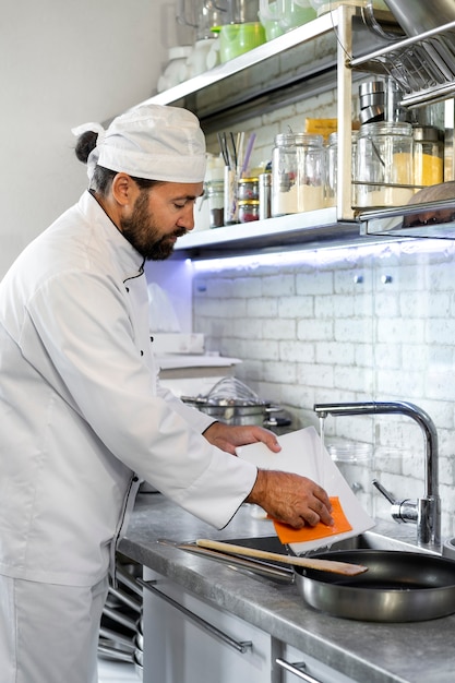 Free photo male chef in the kitchen washing frying pan