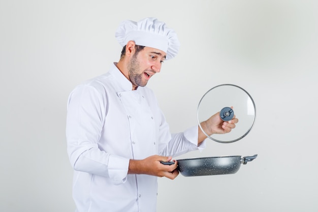 Cuoco unico maschio che apre il coperchio della padella in uniforme bianca e sembra allegro.