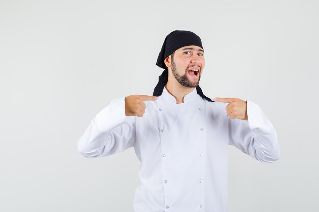 Male chef pointing at himself in white uniform and looking proud. front view.
