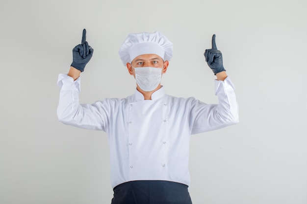 Free photo male chef pointing up fingers in uniform, apron and hat and looking careful