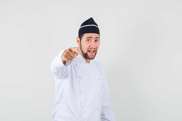 Male chef pointing  in white uniform and looking confident , front view.