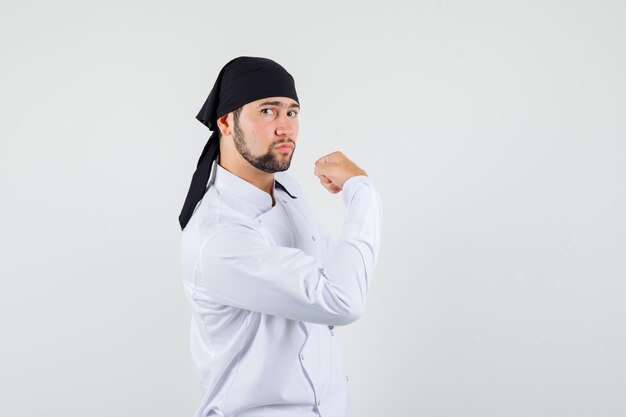 Male chef showing arm muscles in white uniform and looking confident , front view.