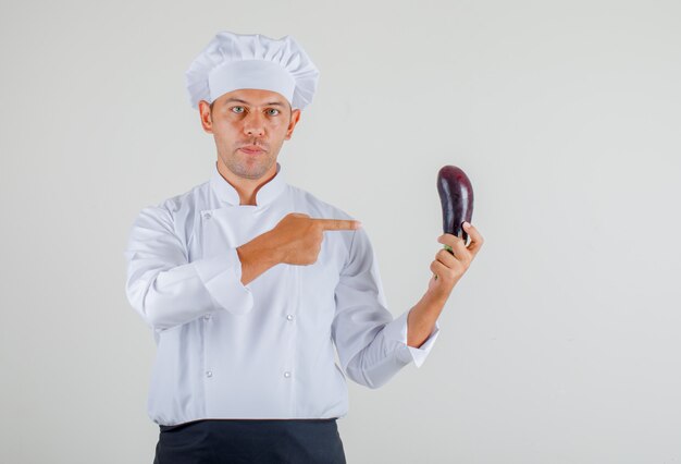 Cuoco unico maschio che mostra melanzana in sua mano in uniforme, grembiule e cappello