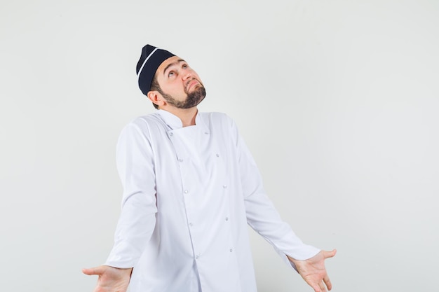 Male chef showing helpless gesture in white uniform and looking sorrowful. front view.