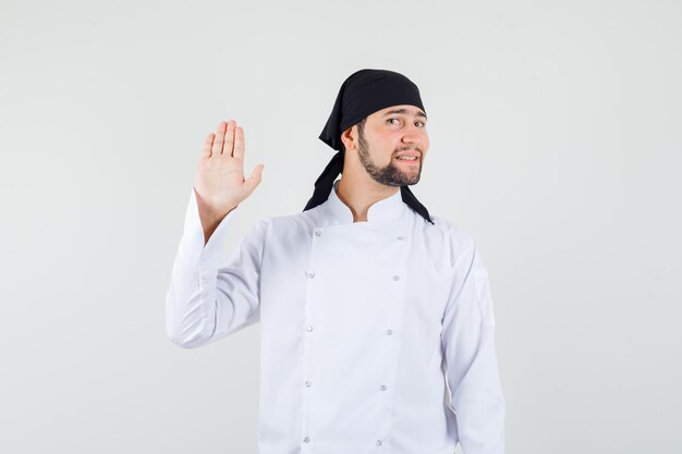 Male chef showing palm in white uniform and looking cheerful , front view.