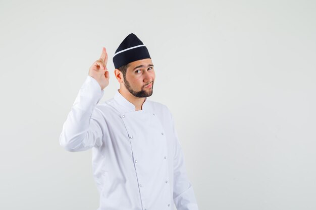 Male chef showing pistol gesture in white uniform and looking brave. front view.