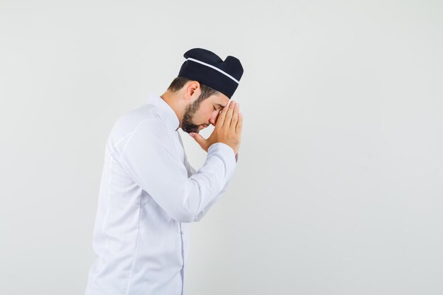 Male chef showing praying gesture in white uniform and looking hopeful. .