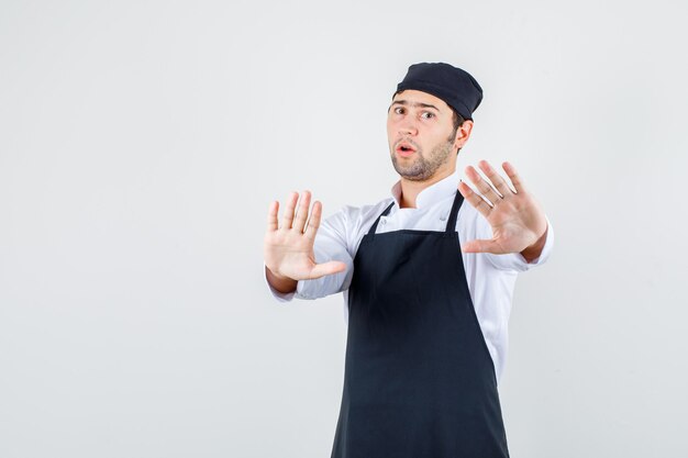 Male chef showing refusal gesture in uniform, apron and looking serious , front view.