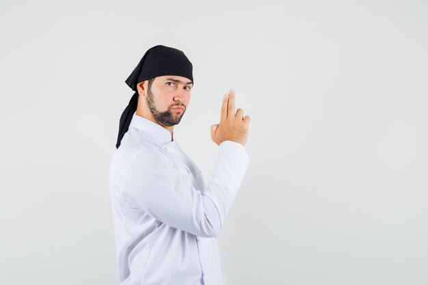 Male chef showing shooting gun gesture in white uniform and looking strict.