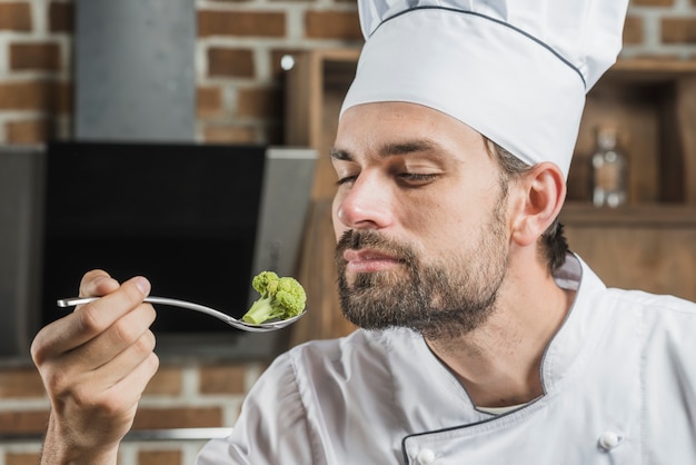 Male chef smelling broccoli in stainless steel spoon