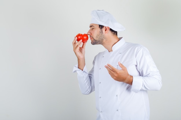 Male chef smelling fresh tomato in white uniform