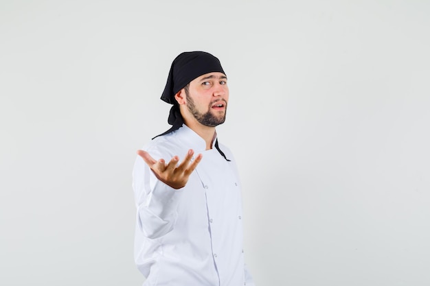 Free photo male chef stretching hand in questioning manner in white uniform and looking confident. front view.