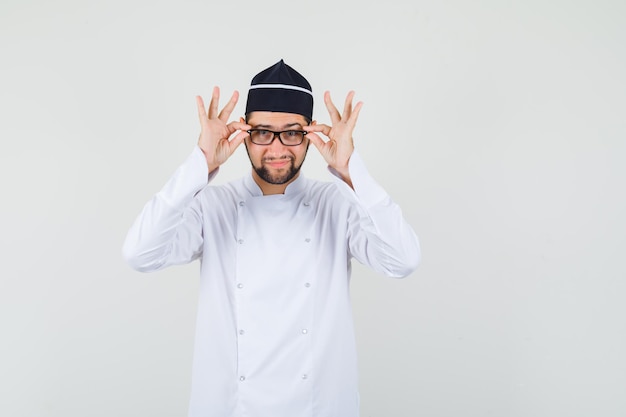Male chef touching his glasses in white uniform and looking positive. front view.