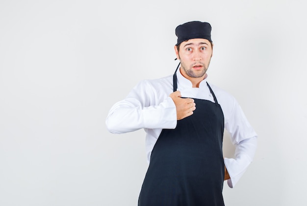 Male chef trying to prove his innocence in uniform, apron and looking puzzled , front view.