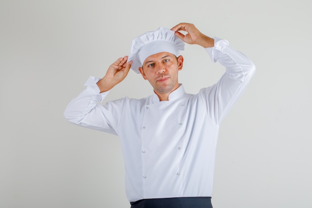 Male chef in uniform, apron and hat posing while holding his hat