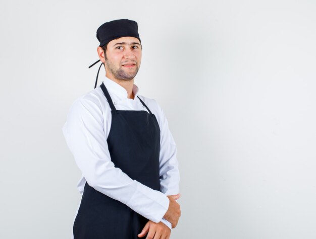 Foto gratuita chef maschio in uniforme, grembiule in piedi e guardando allegro, vista frontale.