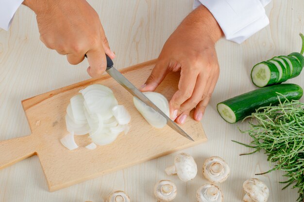 Male chef in uniform chopping onion on cutting board in kitchen