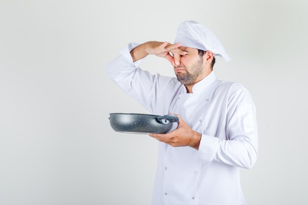 Male chef in white uniform holding bad dish and closing his nose
