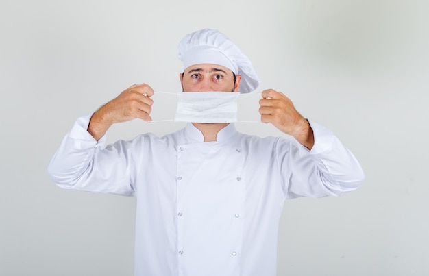 Male chef in white uniform holding medical mask over mouth