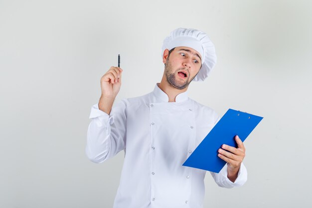 Male chef in white uniform holding pen and clipboard and looking busy