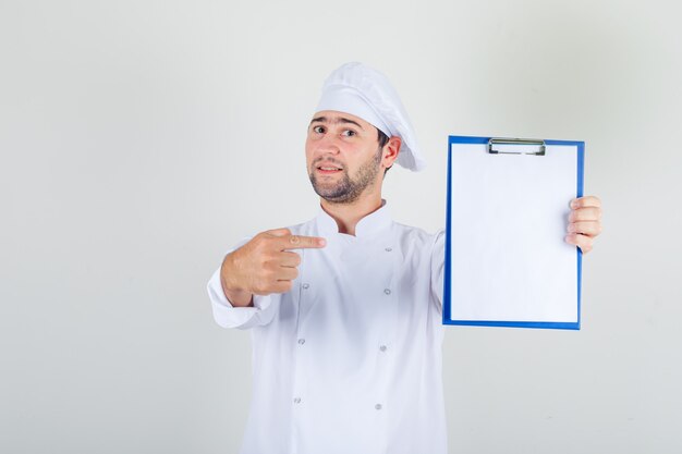 Male chef in white uniform pointing finger at clipboard and looking glad