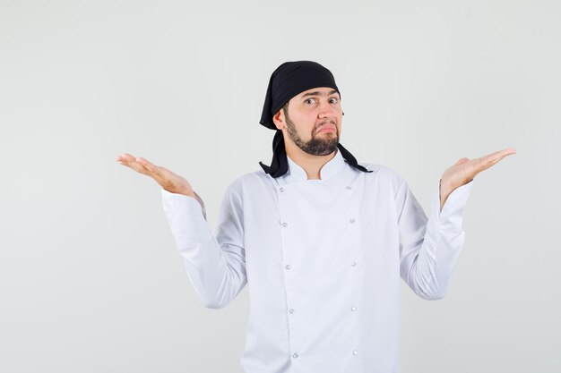 Male chef in white uniform showing helpless gesture and looking confused , front view.