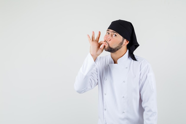 Male chef in white uniform showing zip gesture and looking careful , front view.