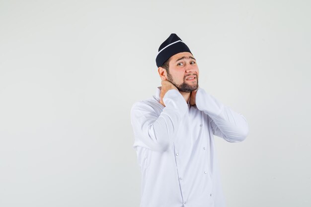 Male chef in white uniform suffering from neck pain and looking uncomfortable , front view.