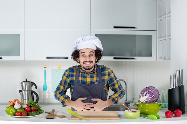 Male chef with fresh vegetables and cooking with kitchen tools and suffering from stomach ache in the white kitchen