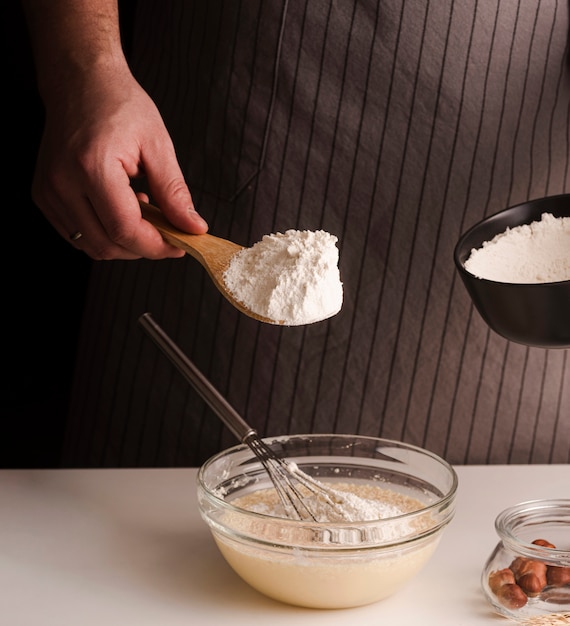 Free photo male cook adding flour to mixture