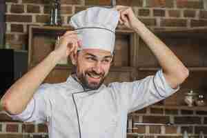 Foto gratuita cuoco maschio che regola il cappello del suo chef bianco sulla sua testa