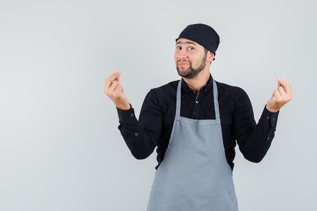 Free photo male cook gesturing with fingers in shirt, apron and looking cheerful , front view.