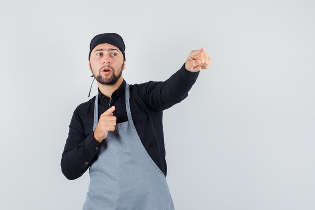 Male cook pointing away in shirt, apron and looking focused. front view.