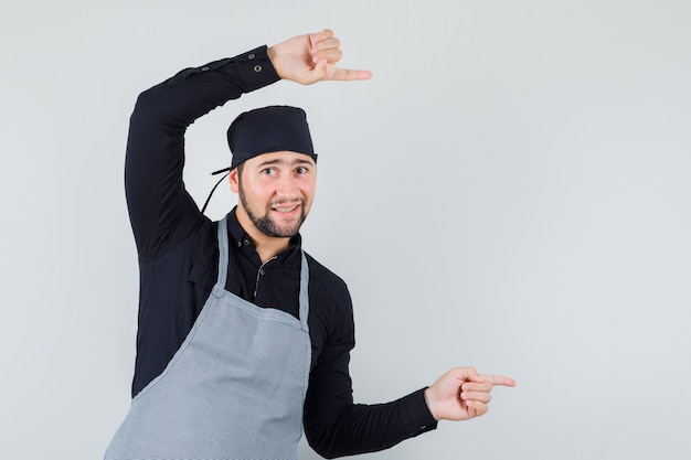 Male cook pointing to the side and smiling in shirt, apron , front view.