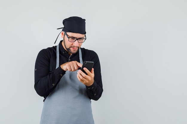 Мужчина повар в рубашке, фартук печатает на мобильном телефоне и выглядит занятым, вид спереди.