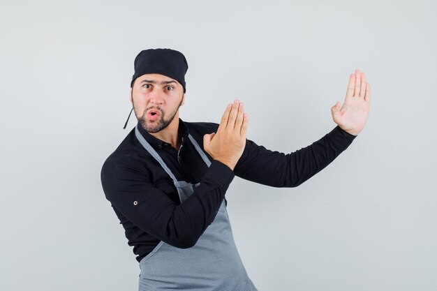 Male cook showing karate chop gesture in shirt, apron and looking angry. front view.