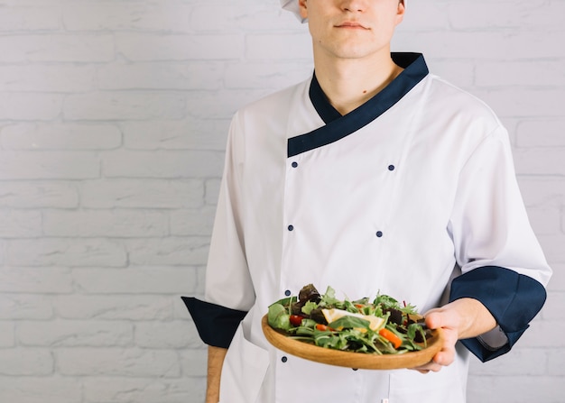 Male cook standing with wooden plate with salad 