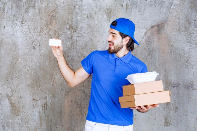Курьер-мужчина в синей форме, несущий картонные и пластиковые коробки и представляющий свою визитную карточку