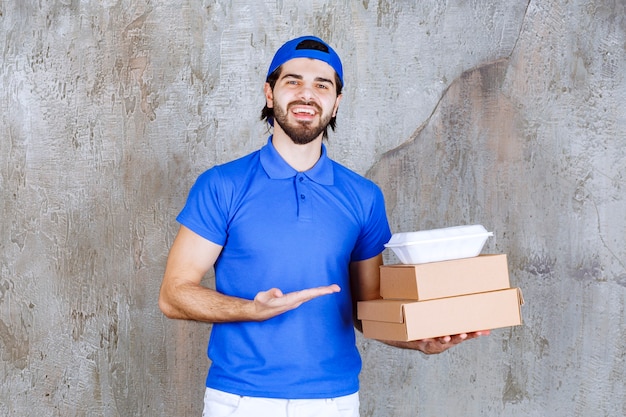 Курьер-мужчина в синей форме несет картонные и пластиковые коробки.