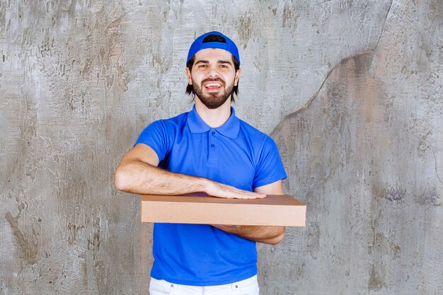 Male courier in blue uniform carrying a cardboard takeaway box .