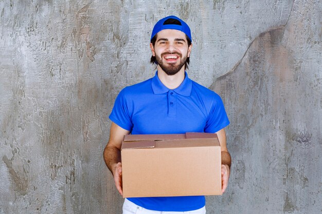 Male courier in blue uniform carrying a cardboard takeaway box . 