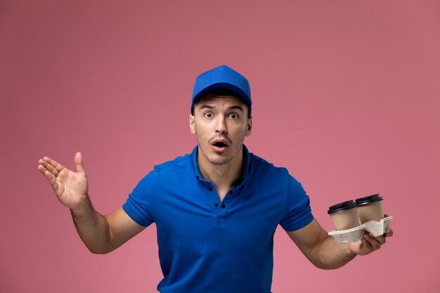 ピンク、労働者の制服サービスの提供に感情的に茶色のコーヒーカップを保持している青い制服の男性宅配便