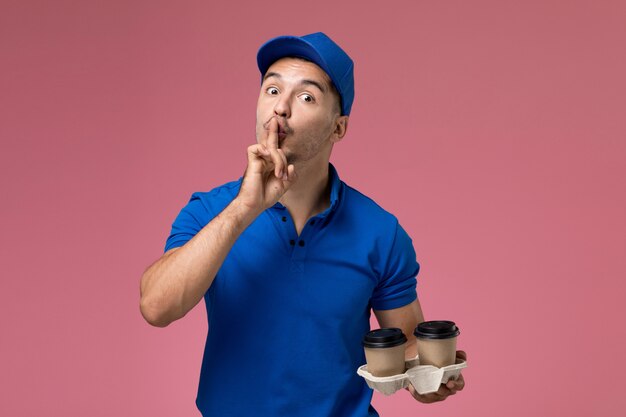 ピンクの沈黙のサインを示す茶色のコーヒーカップを保持している青い制服を着た男性の宅配便、労働者の制服サービスの提供