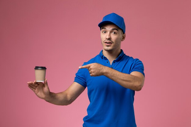 курьер-мужчина в синей форме держит чашку кофе на розовом, униформа службы доставки