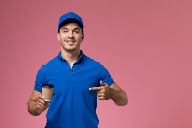 male courier in blue uniform holding coffee cup and smiling on pink, worker uniform service delivery