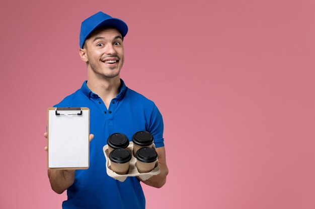 male courier in blue uniform holding coffee cups and notepad on pink, worker uniform service delivery