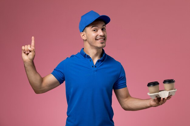 курьер-мужчина в синей униформе держит кофейные чашки, улыбаясь розовому, служба доставки униформы