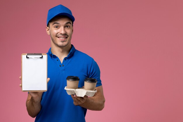 male courier in blue uniform holding coffee with smile on pink, worker uniform service delivery