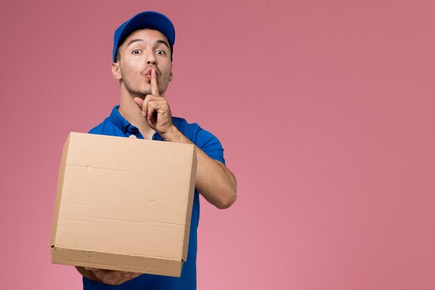 курьер-мужчина в синей форме держит коробку с доставкой еды, открывая ее на розовом, доставка униформы рабочего