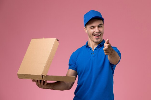 Corriere maschio in uniforme blu che tiene la scatola di consegna del cibo aprendolo ammiccante sulla rosa, consegna del servizio uniforme del lavoratore di lavoro